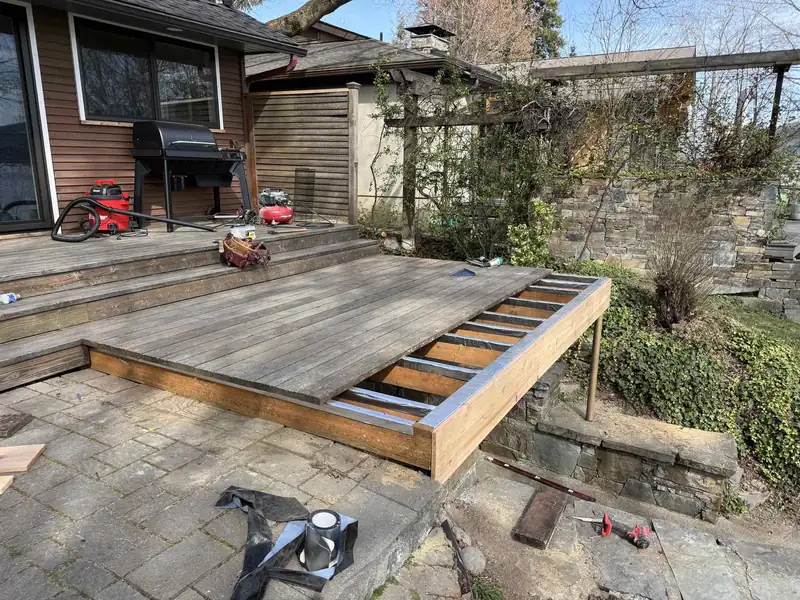 New cantilevered deck extension under construction, framed out over a stone retaining wall and patio