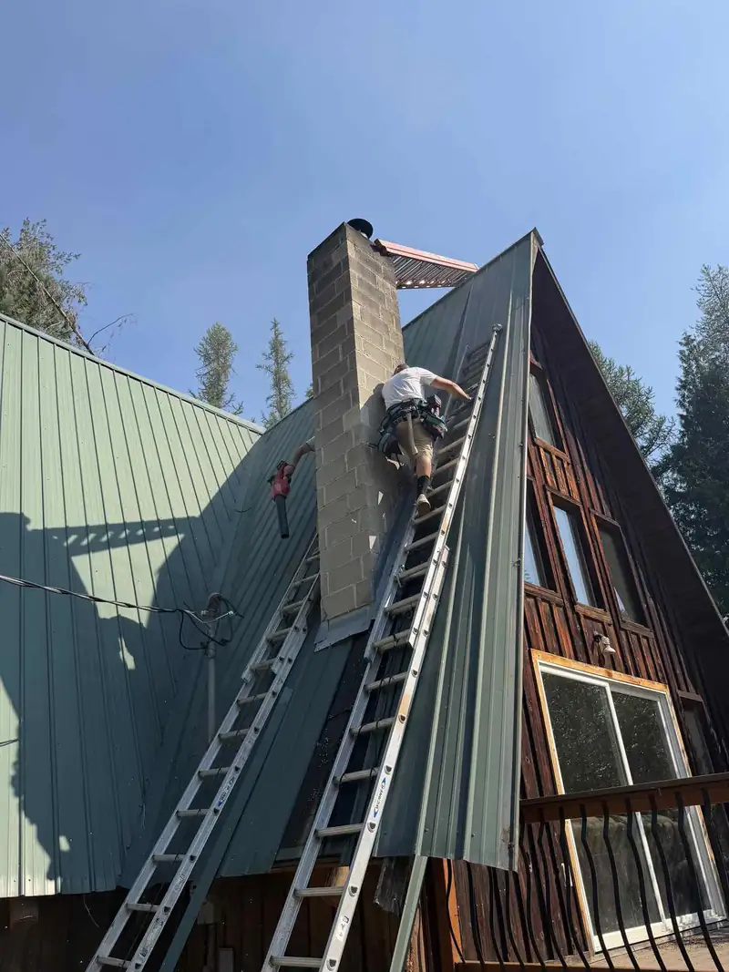7B Handyman crew member on extension ladders working at a chimney and metal roof for gutter clearing