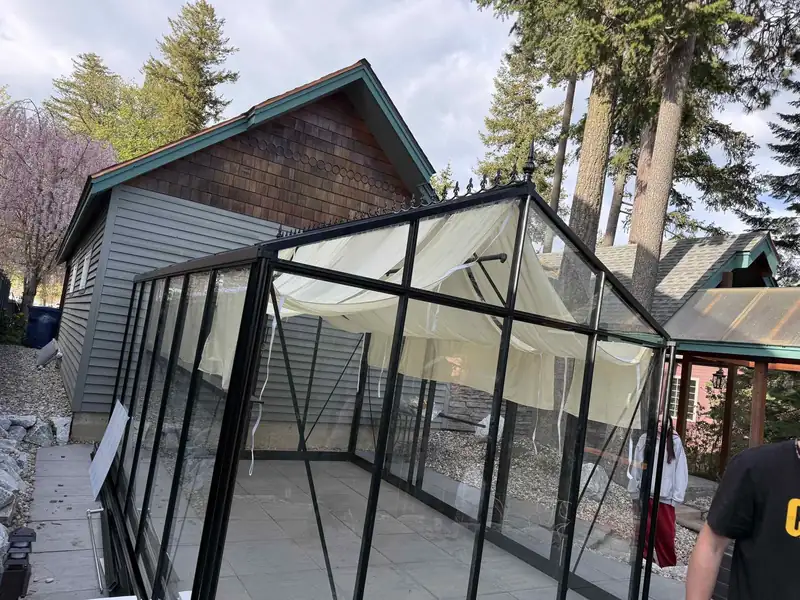 Glass-paneled sunroom addition being installed onto the back of a shingle-sided house